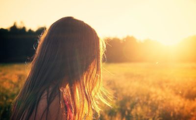 Hon flicka med långt hår som står på ett fält i solnedgången.