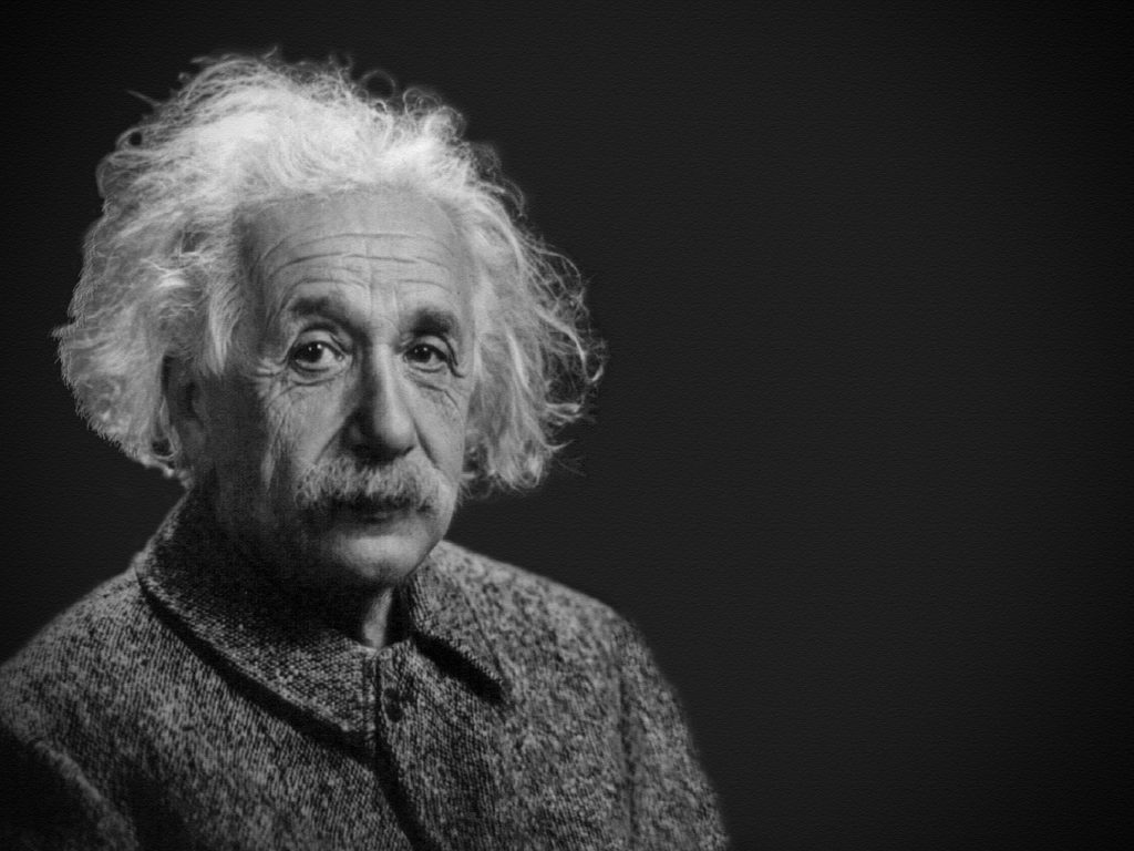 Albert Einstein sitter och tittar mot kameran. Han har stort rufsigt vitt hår, en stor mustasch och ganska många rynkor i pannan. Han ser snäll men lite trött ut.